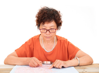 白背景前使用放大镜查看摊在桌子上的地图的中国老太太