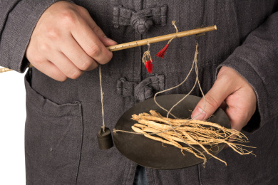 白色背景上,一个成年人穿着中国传统服装拿着一杆秤在称中药