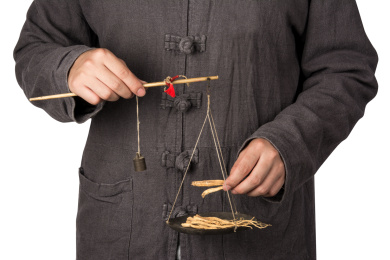 白色背景上,一个成年人穿着中国传统服装拿着一杆秤在称中药