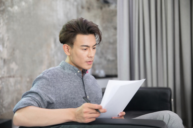 坐在沙发上东方面孔的商务男士正在仔细查看相关文件资料