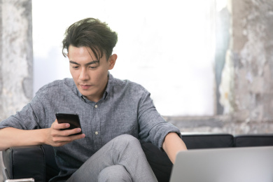 笔记本电脑前坐在沙发上操作手机的商务男士