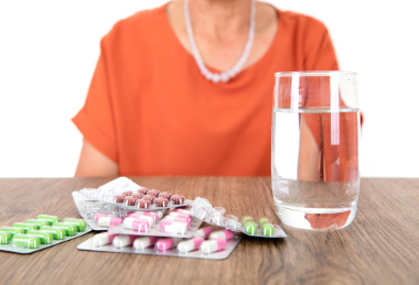 桌子上一杯水和一堆药及坐在桌子旁的中国老太太