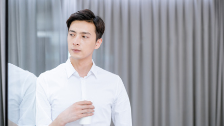 依靠在办公室玻璃墙上喝水休息的中国年轻男性