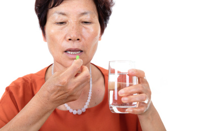 白背景前的中国老太太端着一杯清水正要吃药