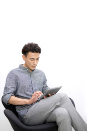 白墙前一位年轻商务男士坐在椅子上使用ipad