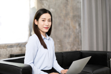 工作中的中国年轻女士坐在沙发上手拿笔记本电脑看着镜头