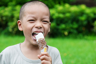 盛夏一位中国男童在公园里绿色草坪上开心地吃冰爽的冰淇淋解暑