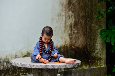 一个两岁的小男孩穿着小和尚的衣服坐在石桌上玩树叶