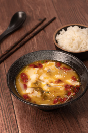 红褐色木板桌面上碗里的酸菜鱼，和旁边的一碗米饭