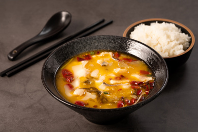 黑色桌面上碗里的酸菜鱼和旁边的一碗米饭