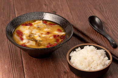 红褐色木板桌面上碗里的酸菜鱼，和旁边的一碗米饭