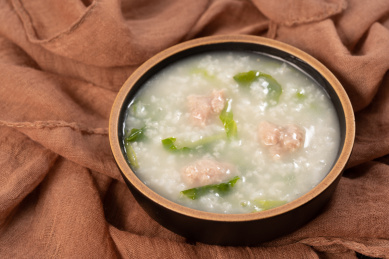 红褐色丝巾上碗里的青菜瘦肉粥