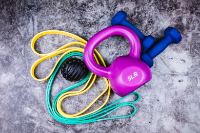 运动主题：正上方视角特写水泥质感地板上放着哑铃壶铃弹力绳和按摩球等运动器械