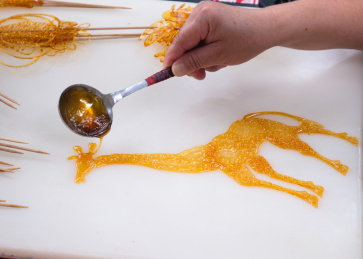 正在白色汉白玉石板上用铁勺乘黄色糖汁绘制的中国民间传统糖画