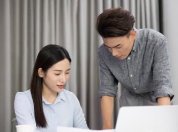 办公室内女工作者和男工作者正在电脑面前讨论问题