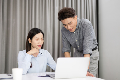 办公室内女工作者和男工作者正在电脑面前讨论问题