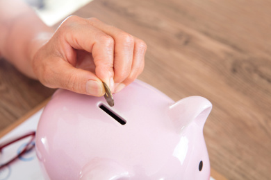 特写拍摄老年人手拿日元硬币正投入小猪存钱罐