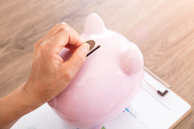 特写拍摄老年人手拿日元硬币正投入小猪存钱罐