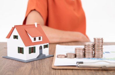 金融文件资料上一排递增的美元硬币和旁边一个小房子模型及坐在桌子旁边的人