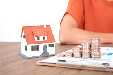 金融文件资料上一排递增的美元硬币和旁边一个小房子模型及坐在桌子旁边的人