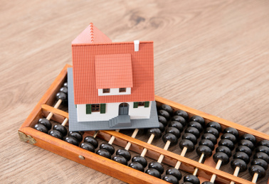 桌子上一个传统计算工具算盘和上面一个小房子模型