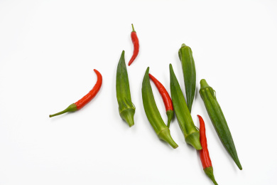 白色背景上随意摆放的绿色蔬菜秋葵及红色小辣椒