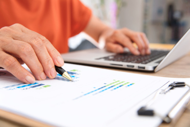 女性工作者边操作笔记本电脑边查看金融资料