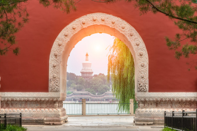 中国北京北海公园夕阳下红墙上的拱门里的白塔