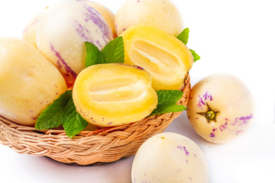 白底上的一筐新鲜人参果上放有两个切开的人参果，篮子下面放有两个完整的人参果