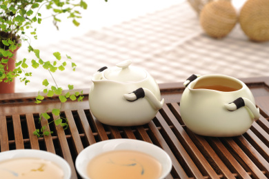 精致的白色瓷器茶壶和茶杯在复古木质茶盘上，冲泡茶叶场景