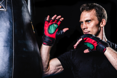 黑色背景特写肌肉线条清晰的英俊男性戴着露指手套在打沙包