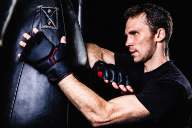 黑色背景特写肌肉线条清晰的英俊男性戴着露指手套在打沙包