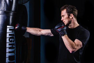 黑色背景特写肌肉线条清晰的英俊男性戴着露指手套在打沙包