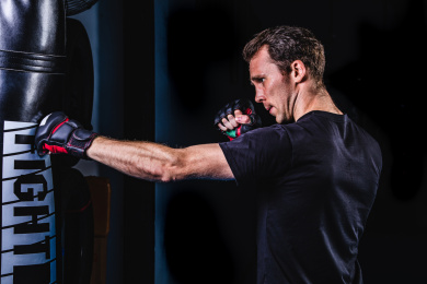 黑色背景特写肌肉线条清晰的英俊男性戴着露指手套在打沙包