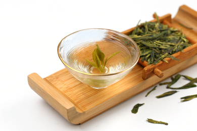 玻璃茶杯斗笠杯里的西湖龙井茶和茶叶放在白色背景上