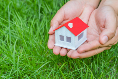 草地背景下捧在手心里的小房子模型