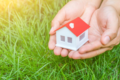 草地背景下捧在手心里的小房子模型