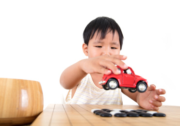 中国小女孩在放着棋子的棋盘上玩小汽车玩具