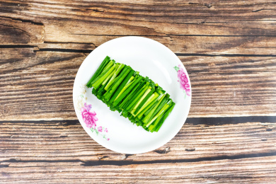 木纹桌子上白色盘子里的绿色韭菜食材