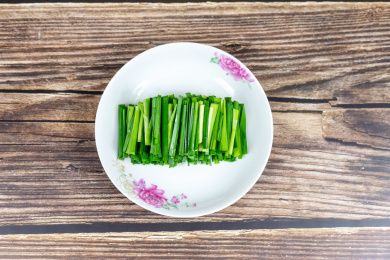 木纹桌子上白色盘子里的绿色韭菜食材