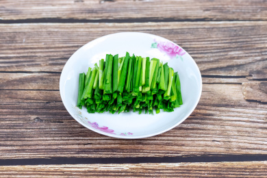 木纹桌子上白色盘子里的绿色韭菜食材