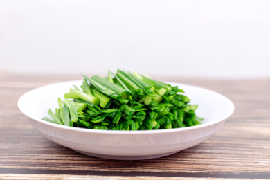 木纹桌子上白色盘子里的绿色韭菜食材