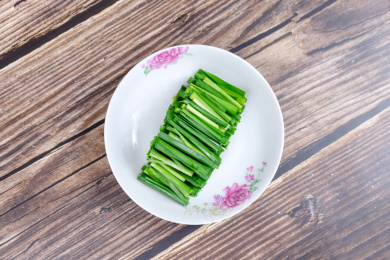 木纹桌子上白色盘子里的绿色韭菜食材