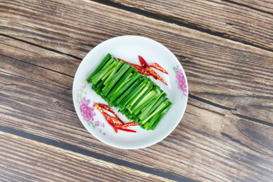 木纹桌子上白色盘子里的绿色韭菜食材