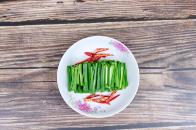 木纹桌子上白色盘子里的绿色韭菜食材