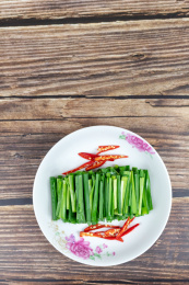 木纹桌子上白色盘子里的绿色韭菜食材