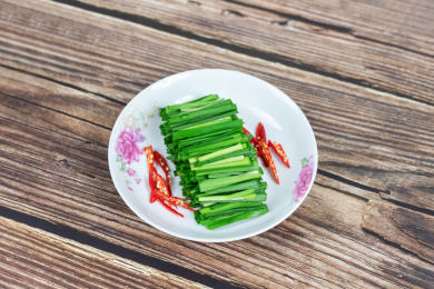 木纹桌子上白色盘子里的绿色韭菜食材