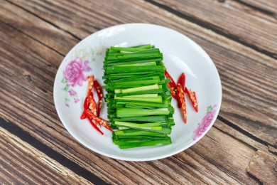 木纹桌子上白色盘子里的绿色韭菜食材