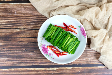 木纹桌子上白色盘子里的绿色韭菜食材