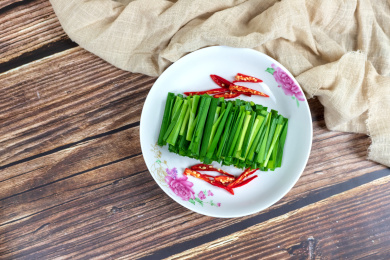 木纹桌子上白色盘子里的绿色韭菜食材